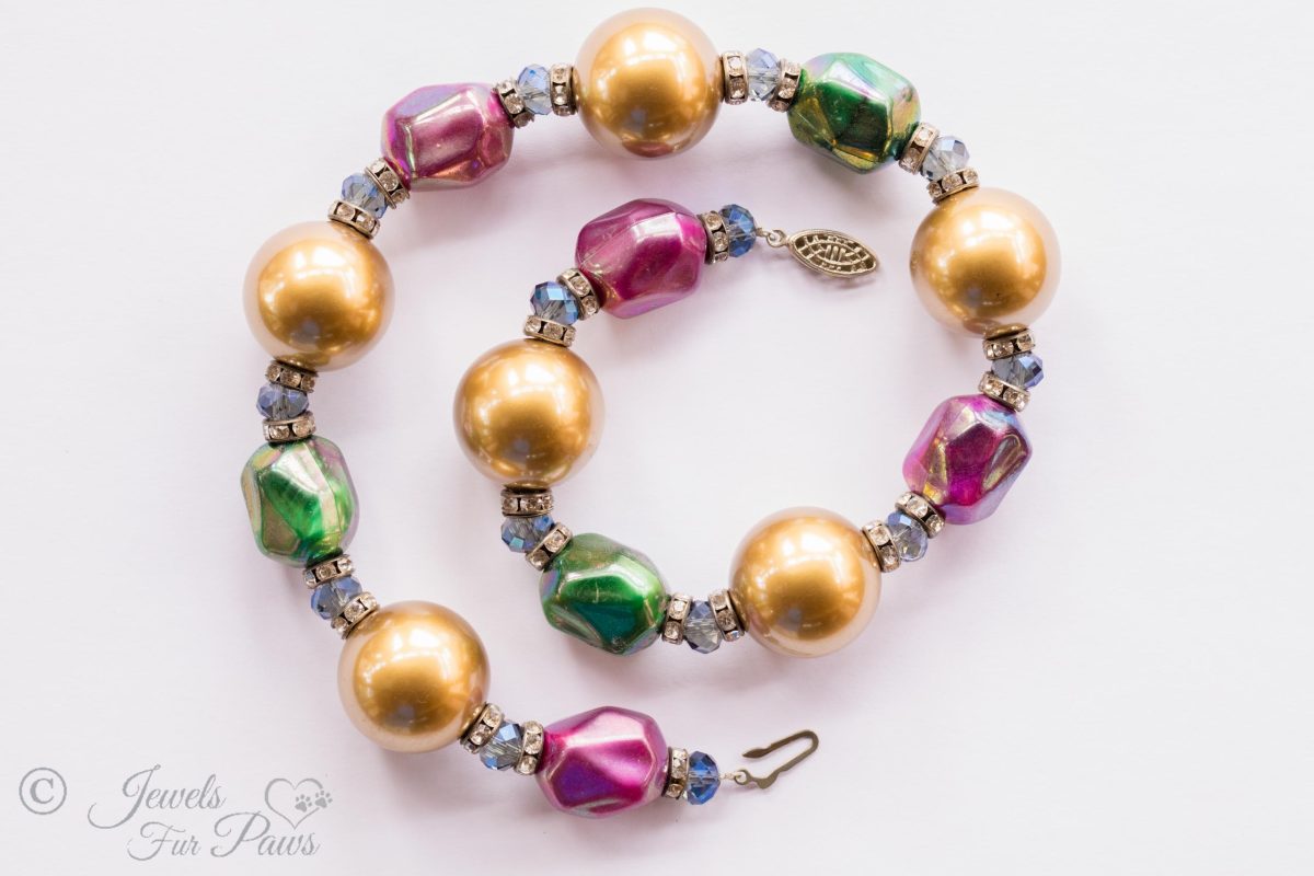 large gold pearl beads with iridescent green and fuchsia pink bauble beads clear swarovski crystal spacers channel set swarovski crystal rhinestone spacers on white background
