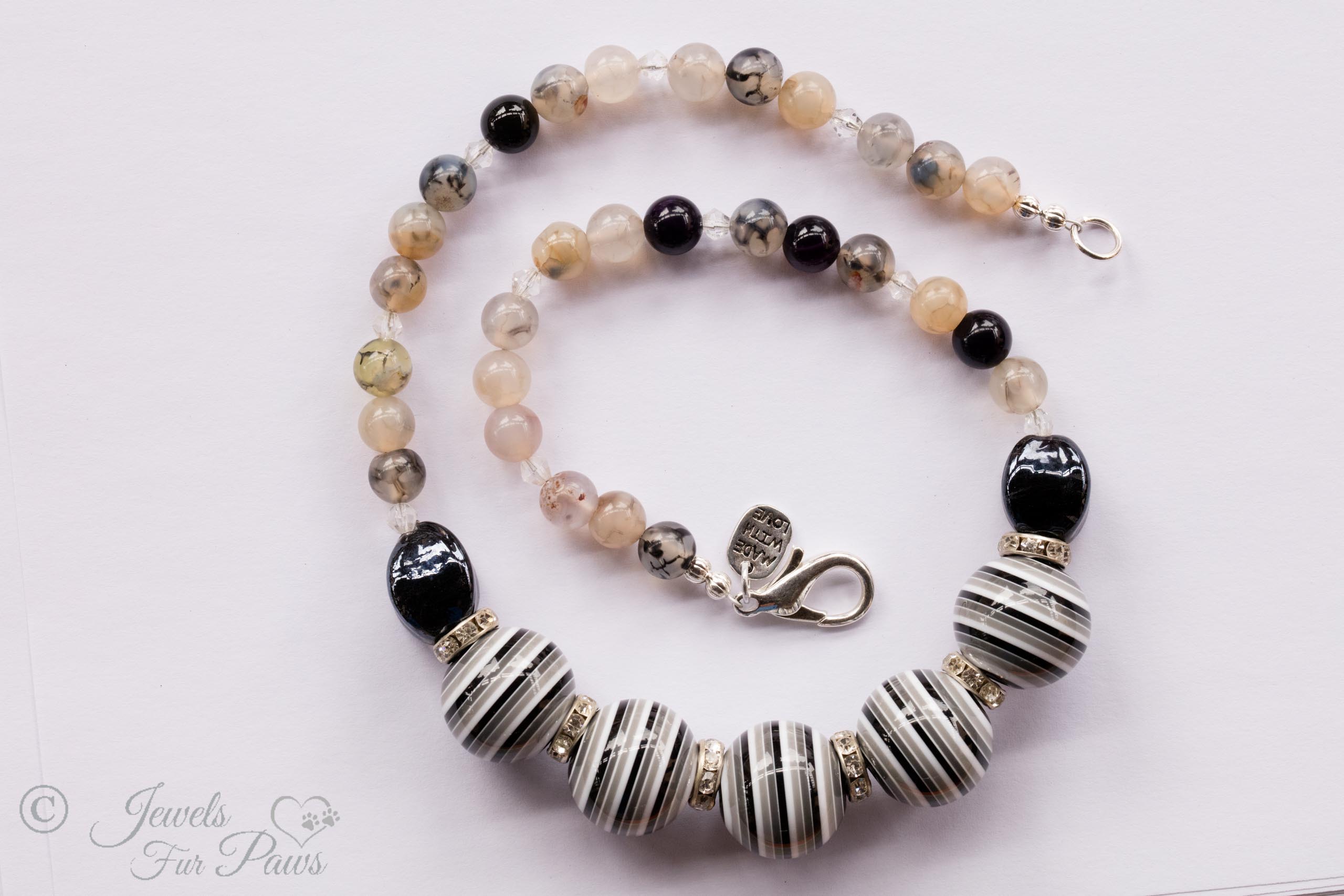black and white striped round beads strung with oval black crystals and marbleized white glass beads on white background