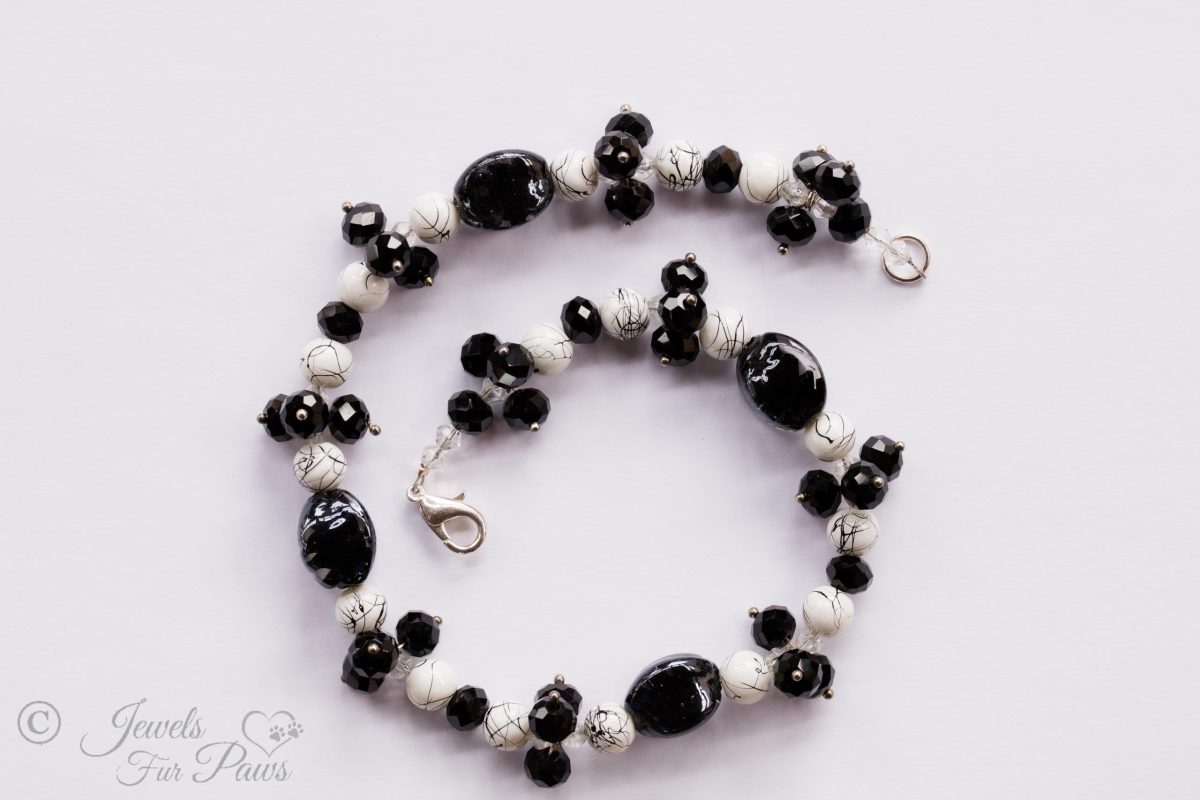 black lampwork oval beads strung with marbleized white and black round beads and faceted Czech crystal clusters on a white background