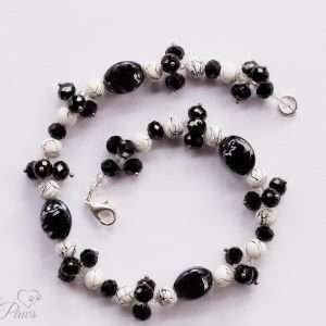 black lampwork oval beads strung with marbleized white and black round beads and faceted Czech crystal clusters on a white background