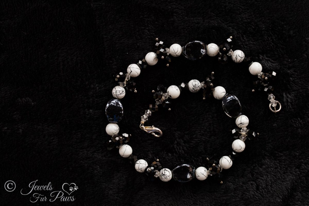 black lampwork oval beads strung with marbleized white and black round beads and faceted Czech crystal clusters on a black background