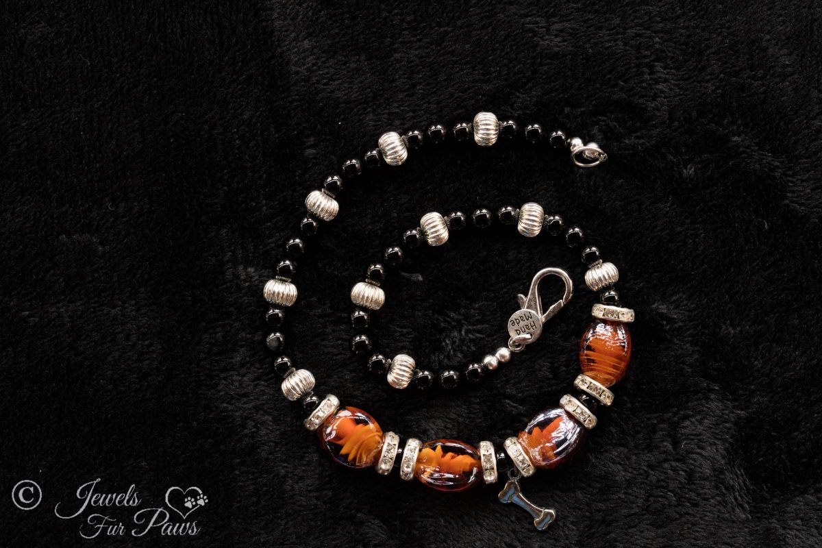 brown lampwork oval glass beads strung with silver rhondell spacers and channel set czech crystal spacers with a hanging silver dog charm on a black background