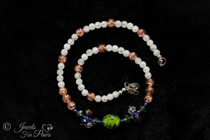 green lampwork glass beads surrounded by green and blue Swarovski crystals and crystal clusters complemented by peach and white cracked glass beads on black background
