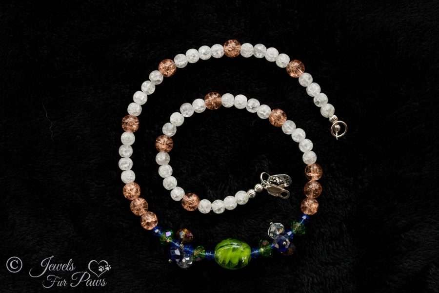 green lampwork glass beads surrounded by green and blue Swarovski crystals and crystal clusters complemented by peach and white cracked glass beads on black background