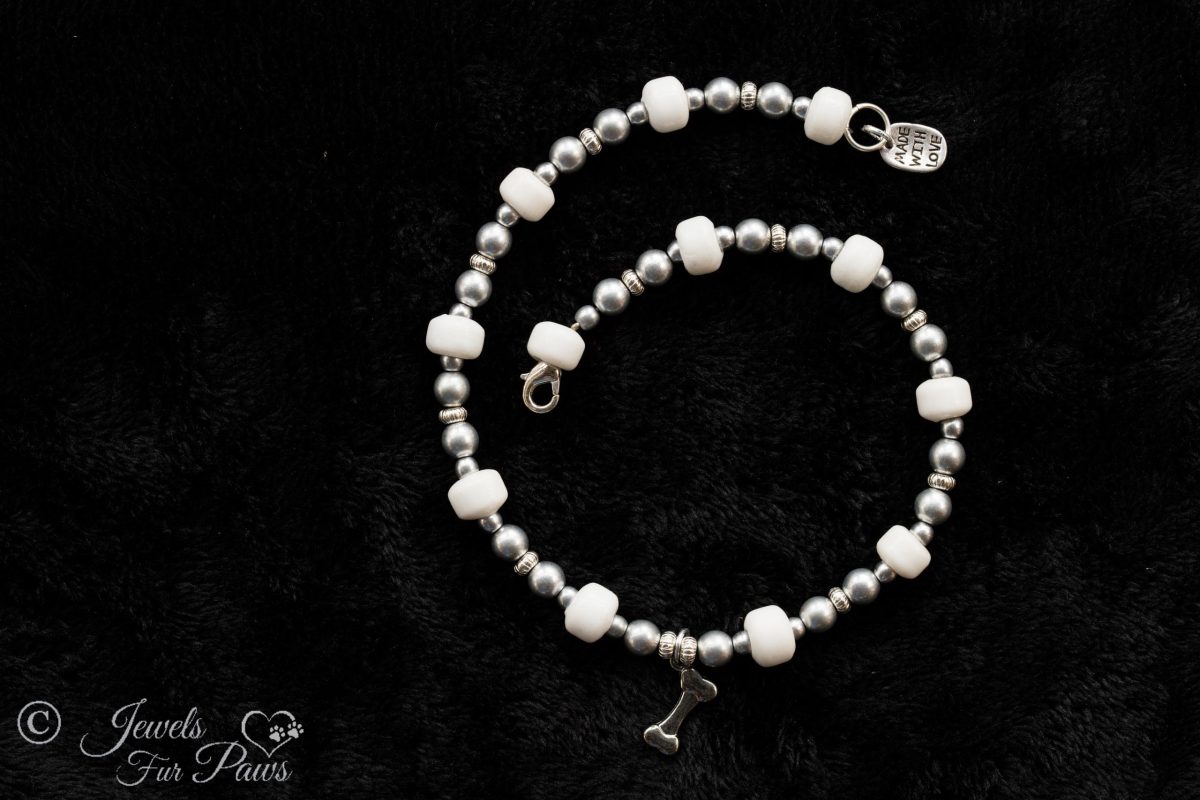 silver hanging bone charm strung with silver beads and larger white glass beads on a black background medium dogs pet necklace jewelry