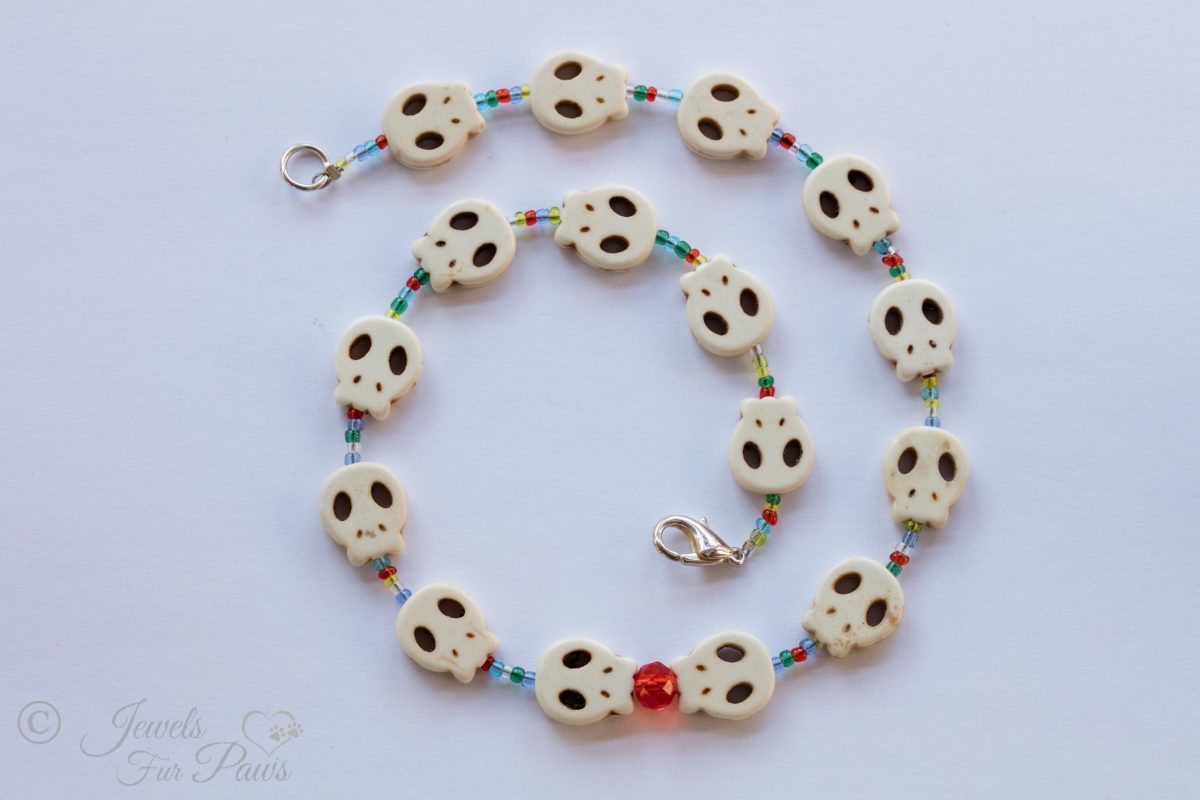 pet dog cat jewelry necklaces white skull charms strung with small blue, green, amber, orange spacer beads and feature a larger faceted red czech crystal on a white background