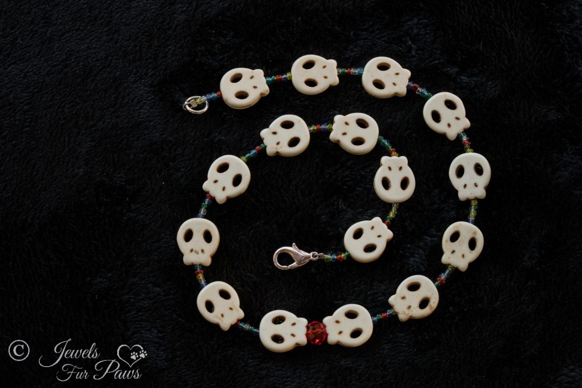 pet dog cat jewelry necklaces white skull charms strung with small blue, green, amber, orange spacer beads and feature a larger faceted red czech crystal on a black background