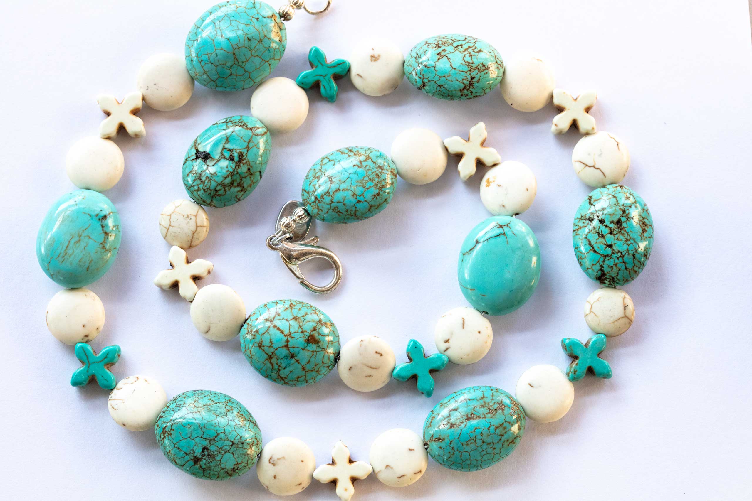 large oval turquoise beads with round flat howlite spacers and turquoise and howlite crosses on white background