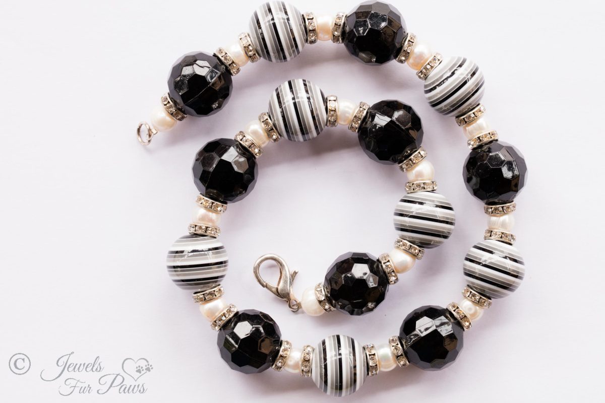 seven large black and white striped round beads with eight round faceted beads and cultured pearls with channel set swarovski crystal rhinestone spacers on white background