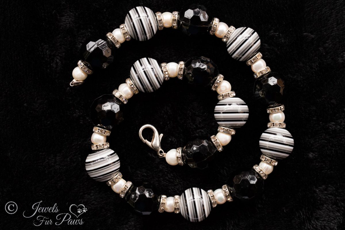 seven large black and white striped round beads with eight round faceted beads and cultured pearls with channel set swarovski crystal rhinestone spacers on black background