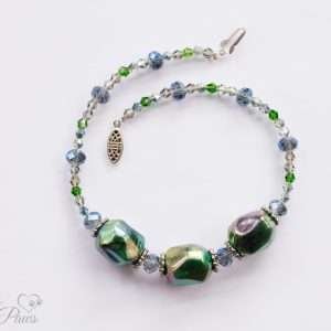 three iridescent green baubles strung with shades of green and blue faceted Czech crystals on a white background