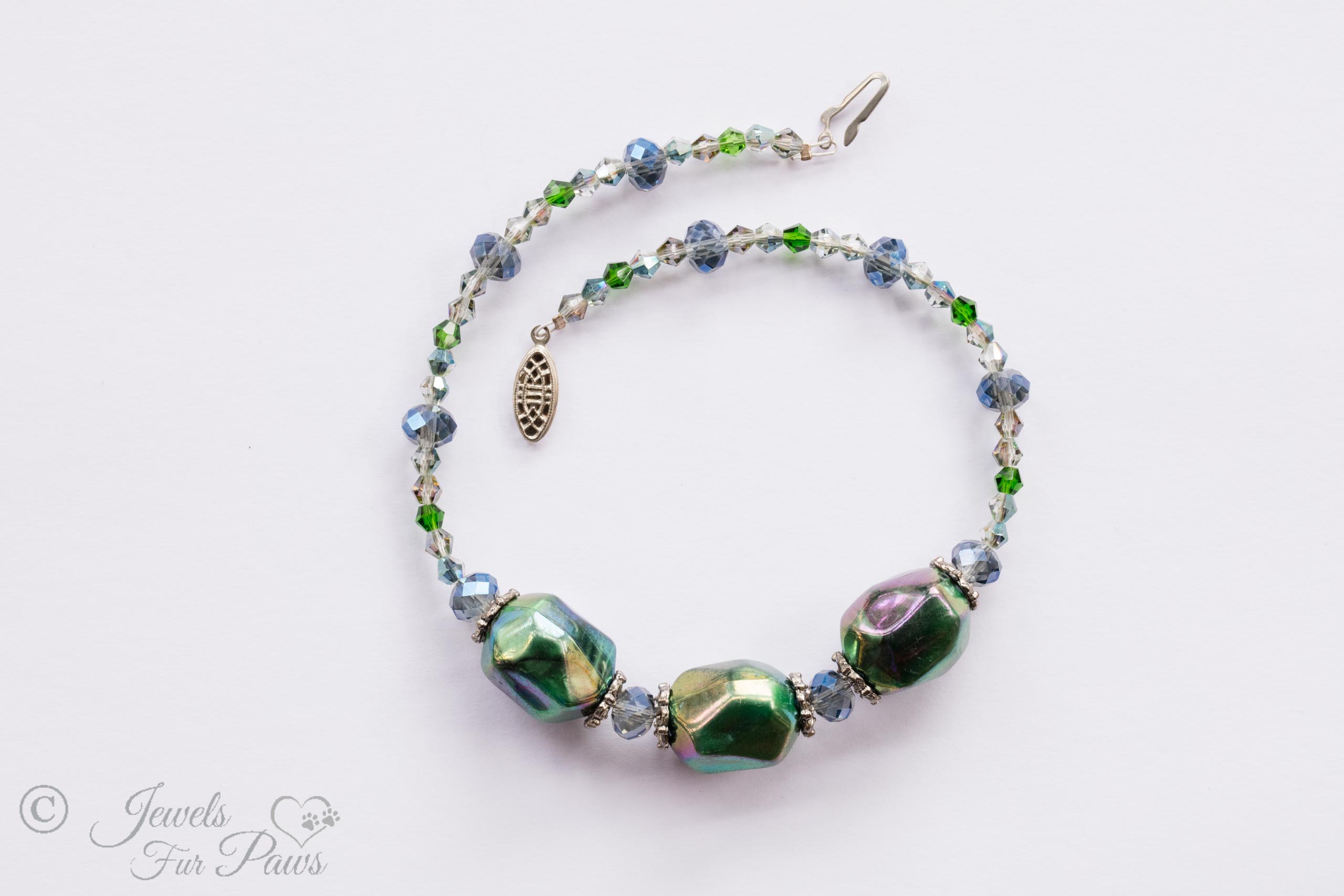 three iridescent green baubles strung with shades of green and blue faceted Czech crystals on a white background