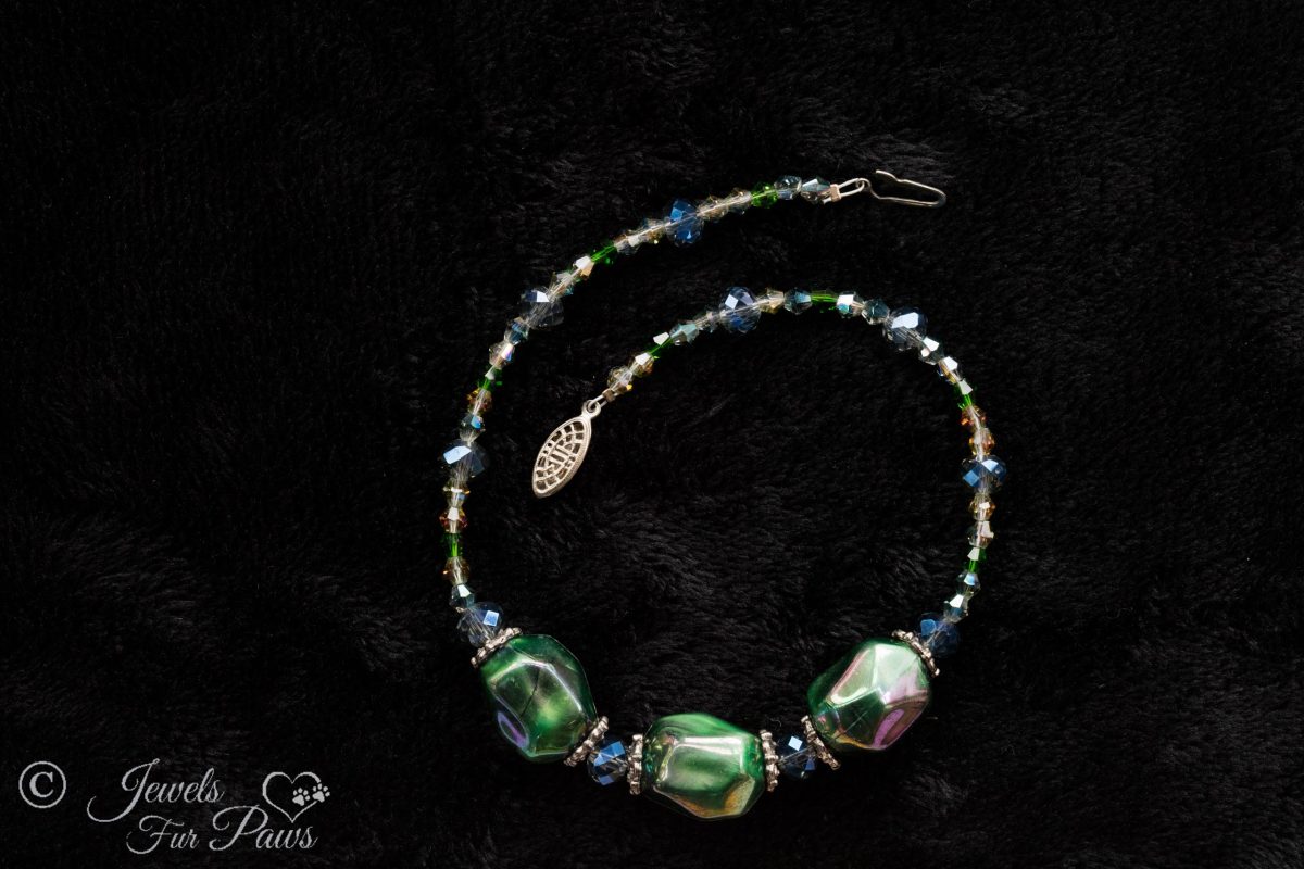 three iridescent green baubles strung with shades of green and blue faceted Czech crystals on a black background