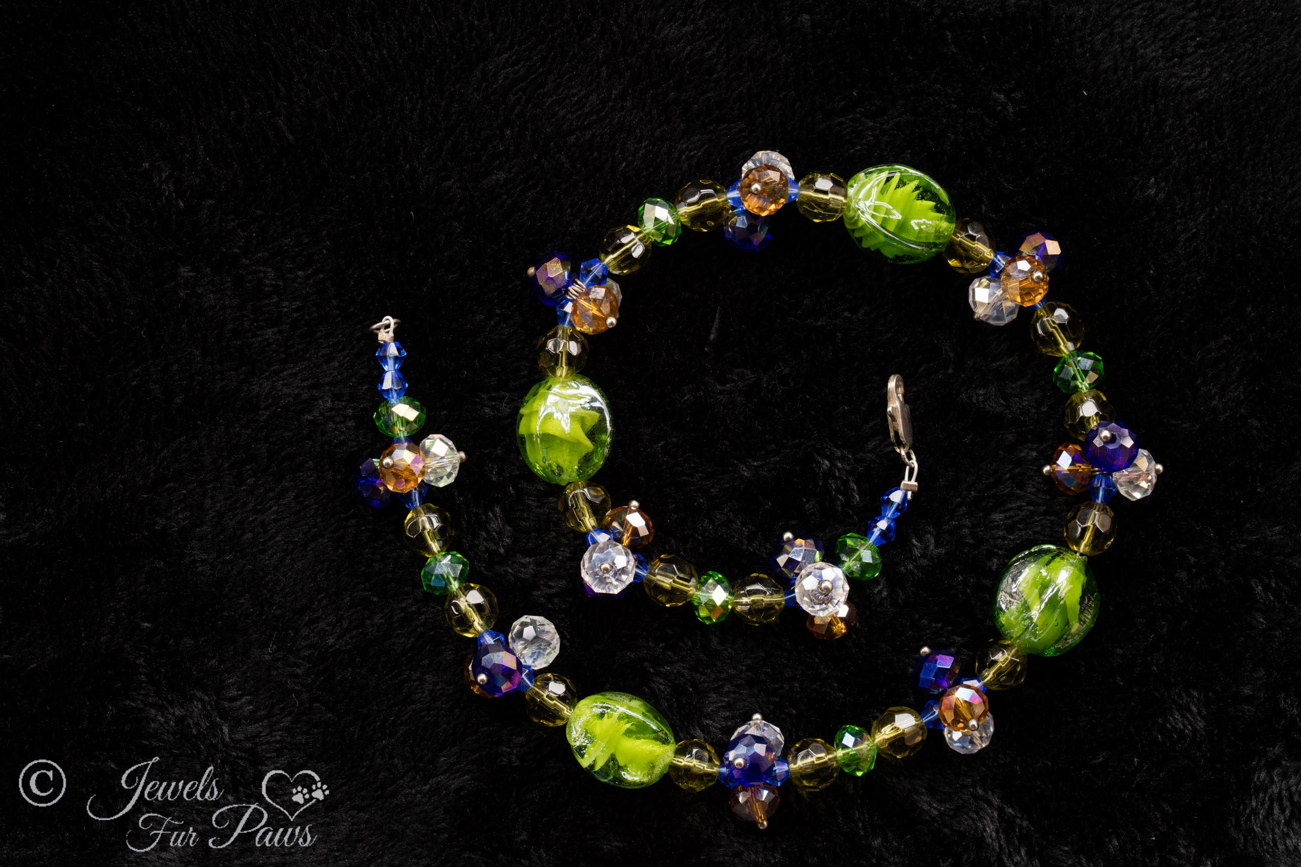 four green lampwork beads with multi-colored swarovski crystals spacer clusters on black background