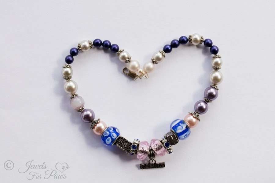 two large faceted pink crystals surround a hanging family charm with pearls, murano crystals on white background