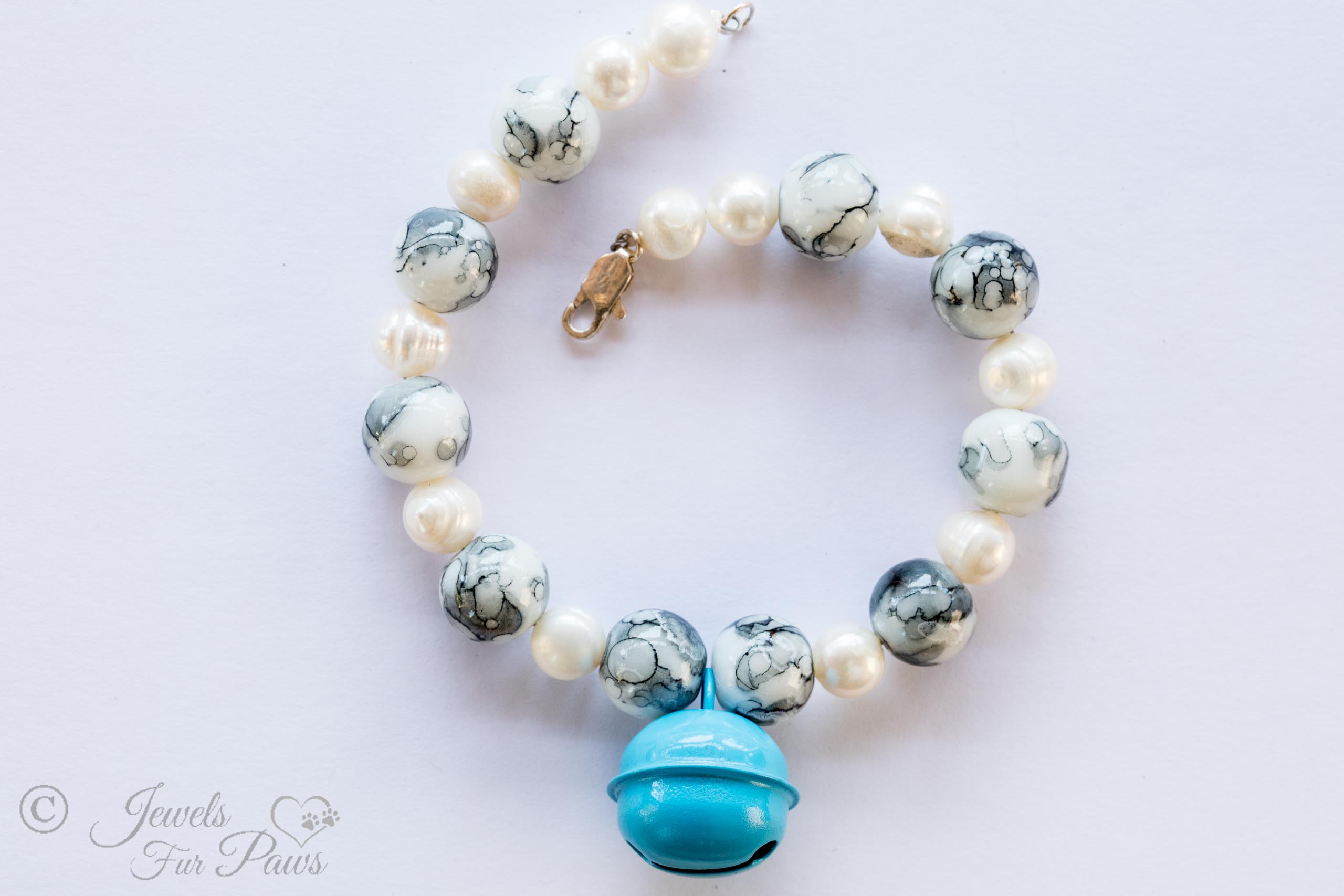 the bell in robin blue pet necklace with pearls and marbelized white and blue beads on white background