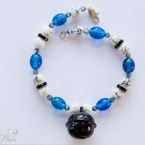 white and black marbleized beads with blue oval crystals and a hanging black bell on white background and black rhinestone spacers