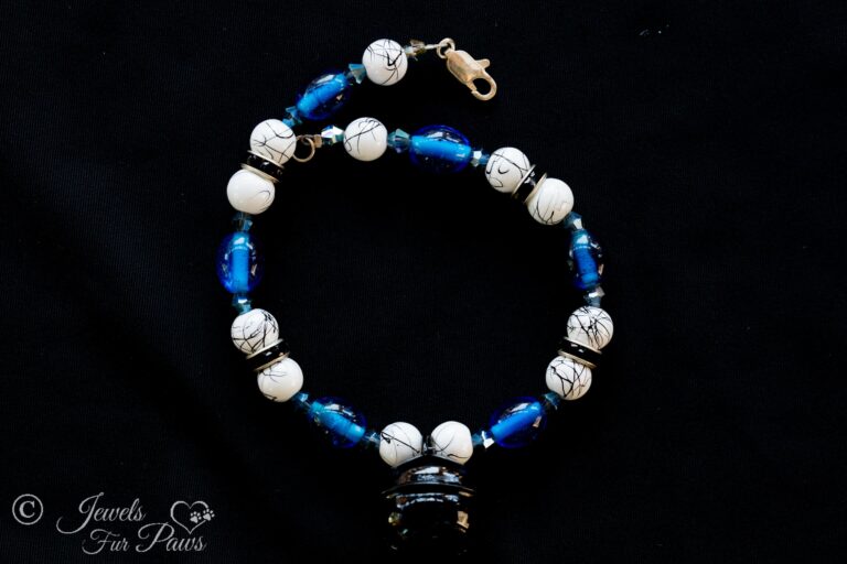 white and black marbleized beads with blue oval crystals and a hanging black bell on black background and black rhinestone spacers