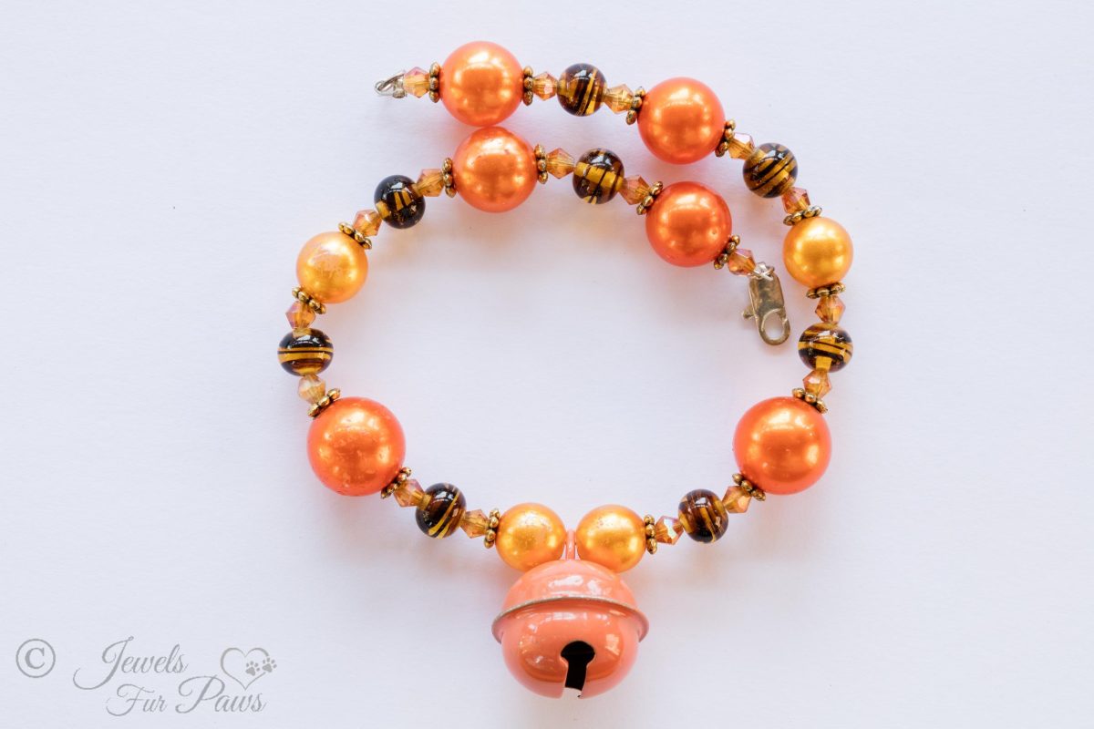 orange pear beads with tigers eye spacers and hanging orange bell on white background