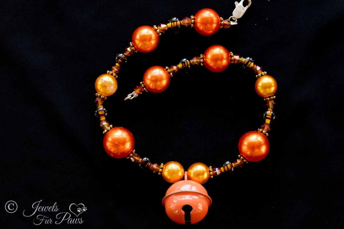 orange pear beads with tigers eye spacers and hanging orange bell on black background
