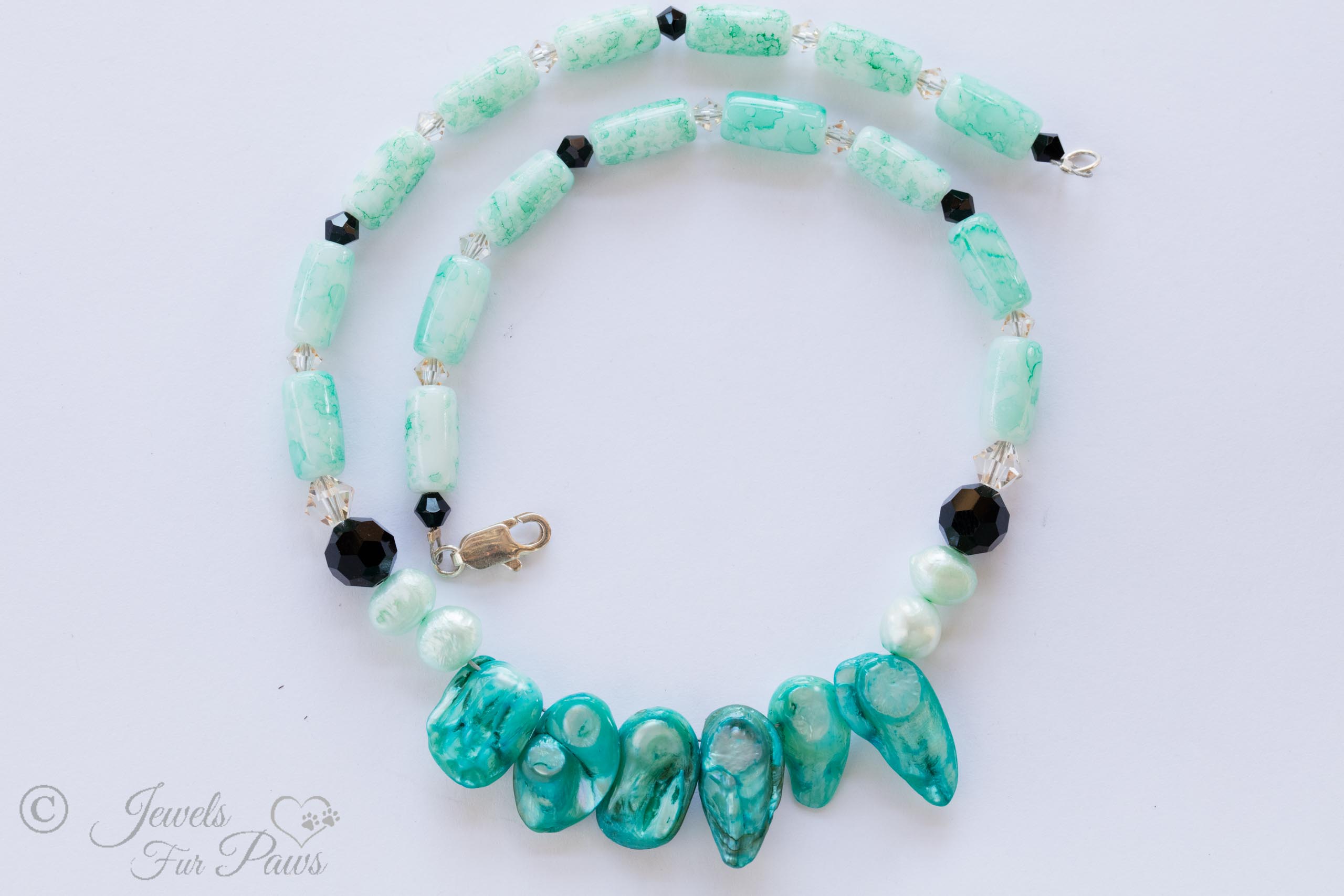 aqua marbleized beads interspersed with black Swarovski crystals complementing five aqua Burmese pearls on a white background