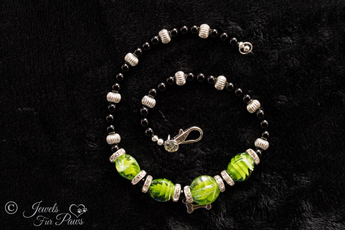 cat dog pet medium necklace four green lampwork glass beads with black onyx beads and fluted silver rondel spacers with channel set swarovski crystals on black background with hanging silver bone charm pendant